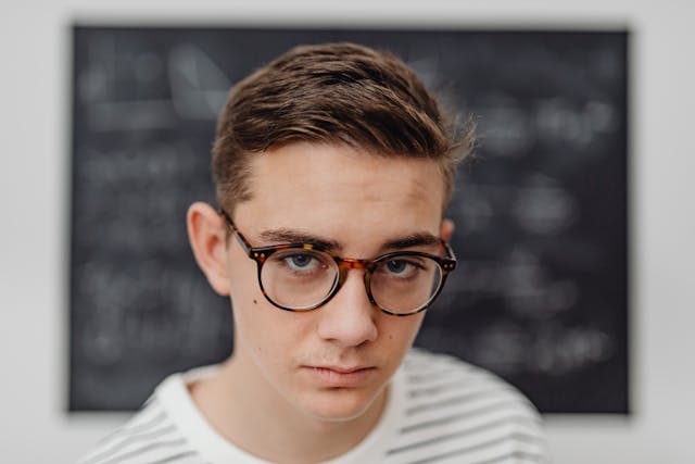 a man wearing glasses in front of a chalkboard